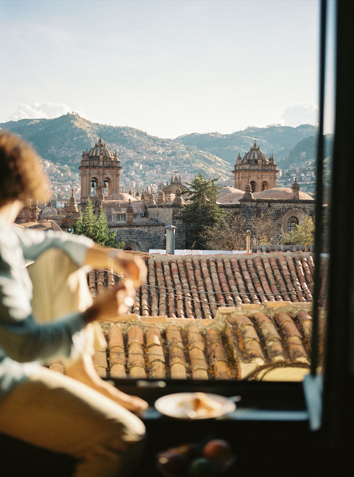 A traveller at an open window above terracotta rooftops and mountains