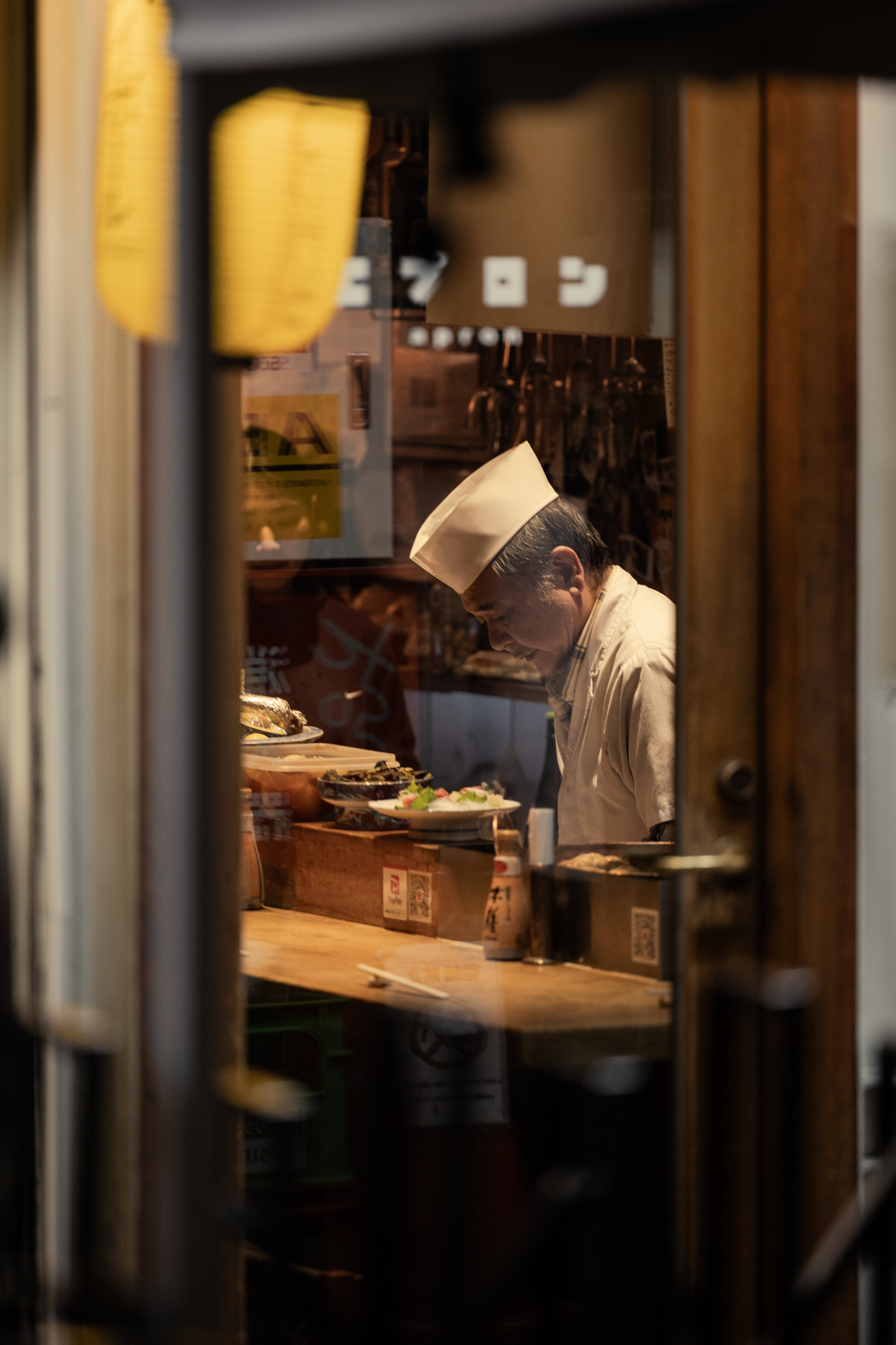 A chef at his counter, seen through the restaurant window