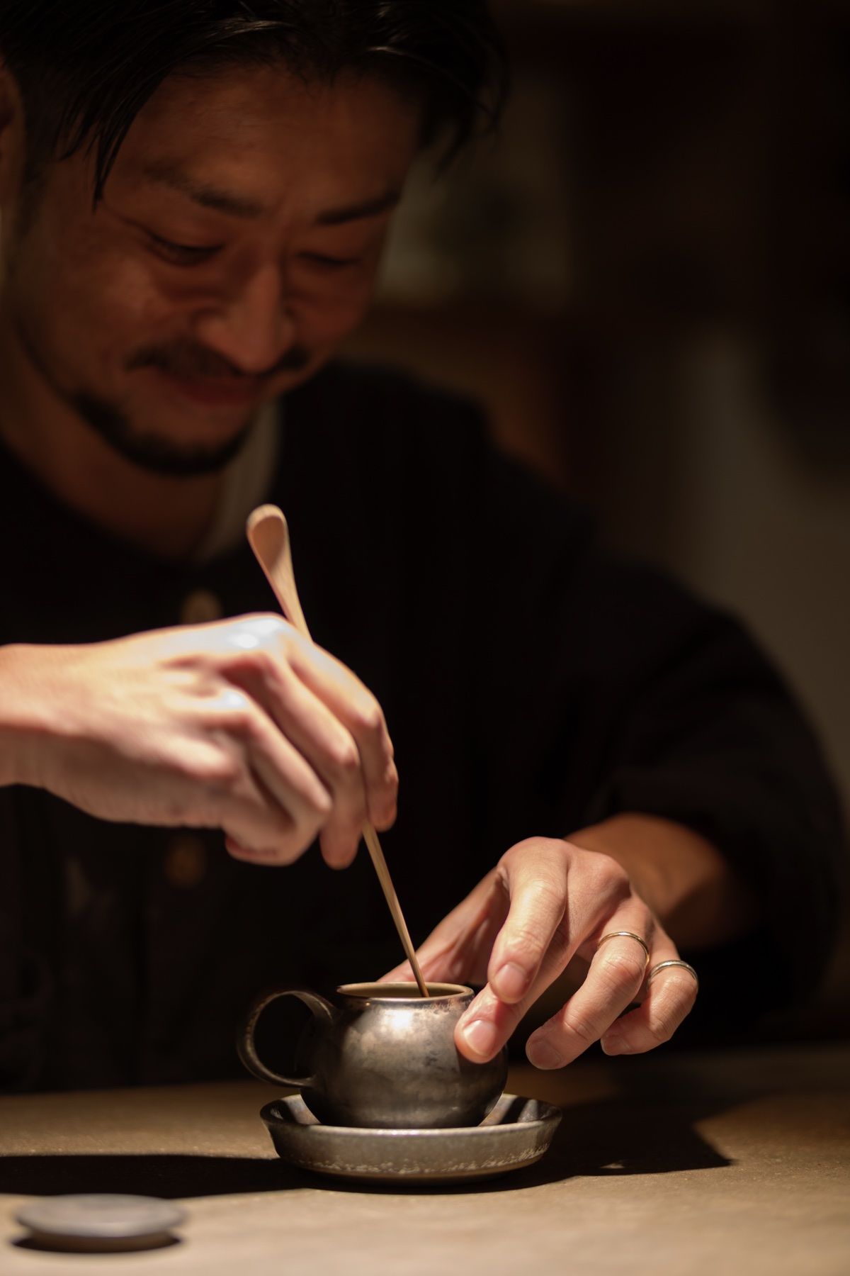 A host whisking tea at a dark counter