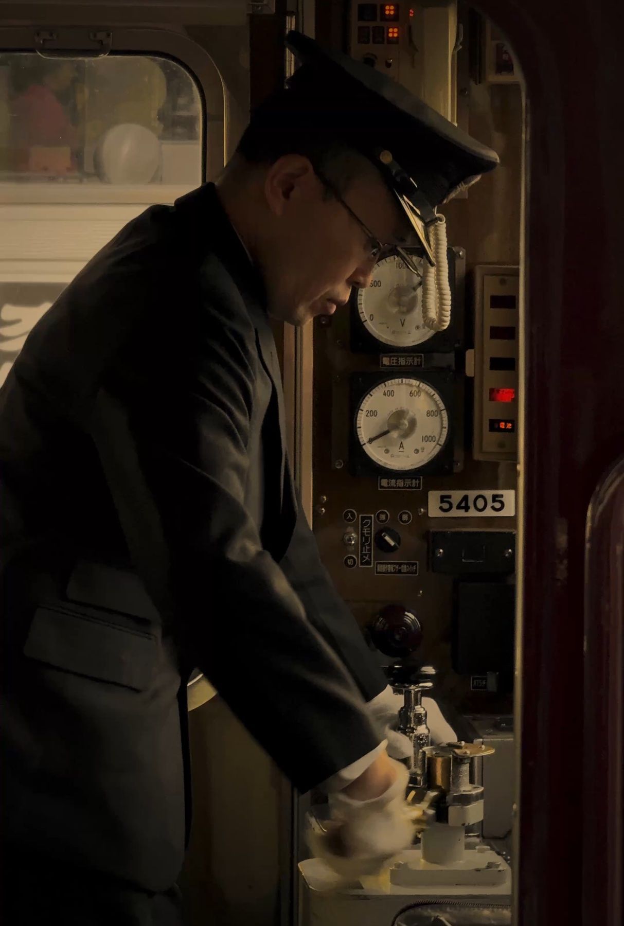 A train conductor at the controls, in uniform and cap