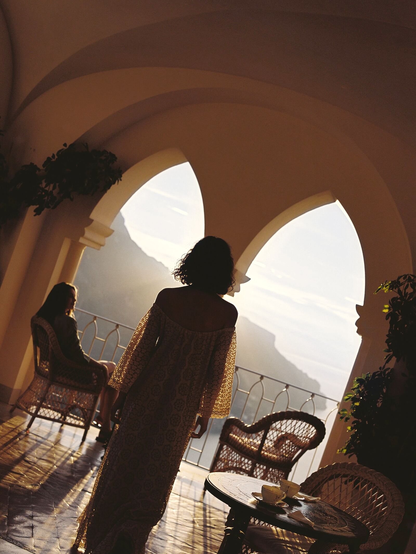A guest on a sunlit terrace between arches, the coast beyond
