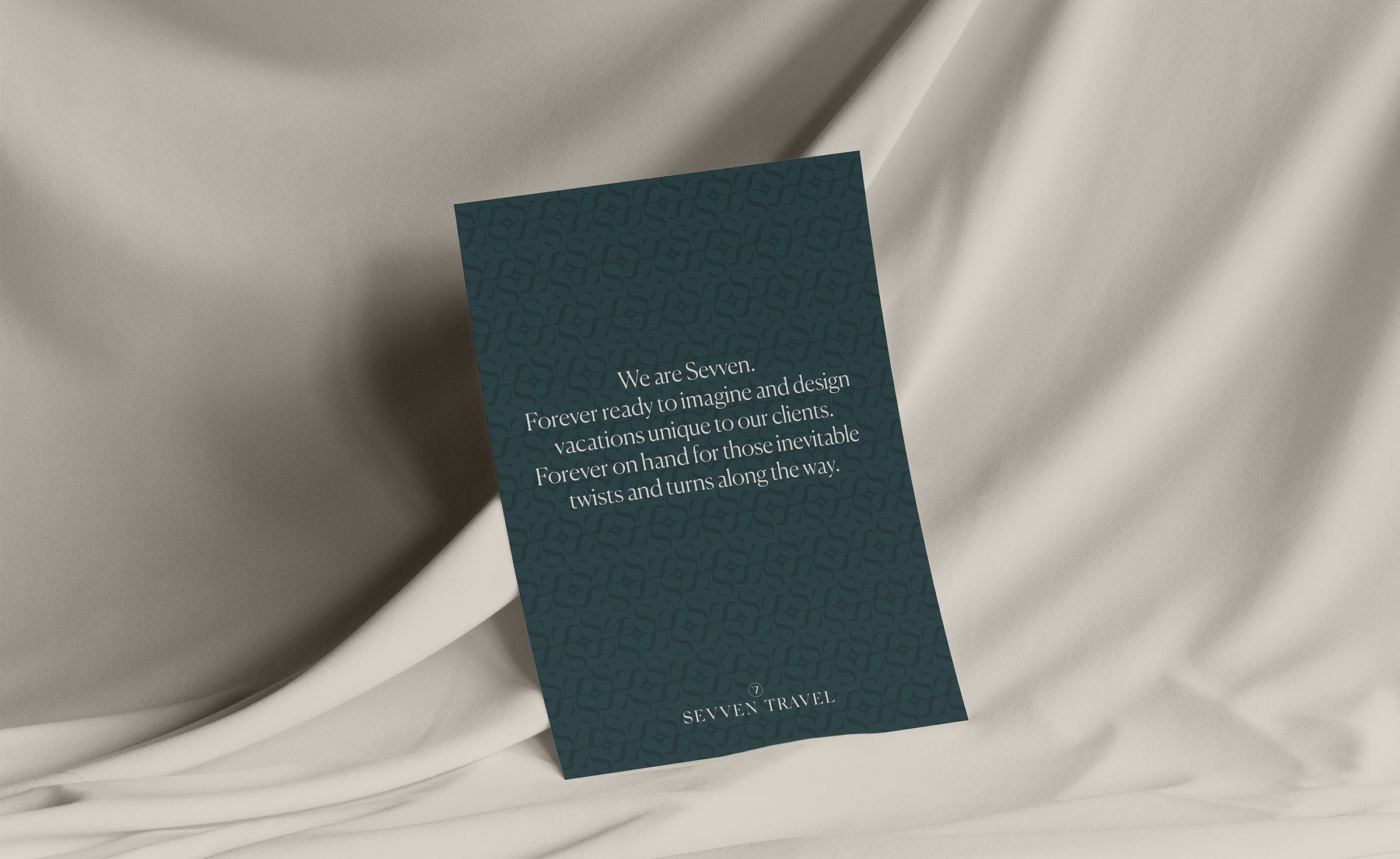 A Sevven Travel card in deep teal reading 'We are Sevven', resting on linen