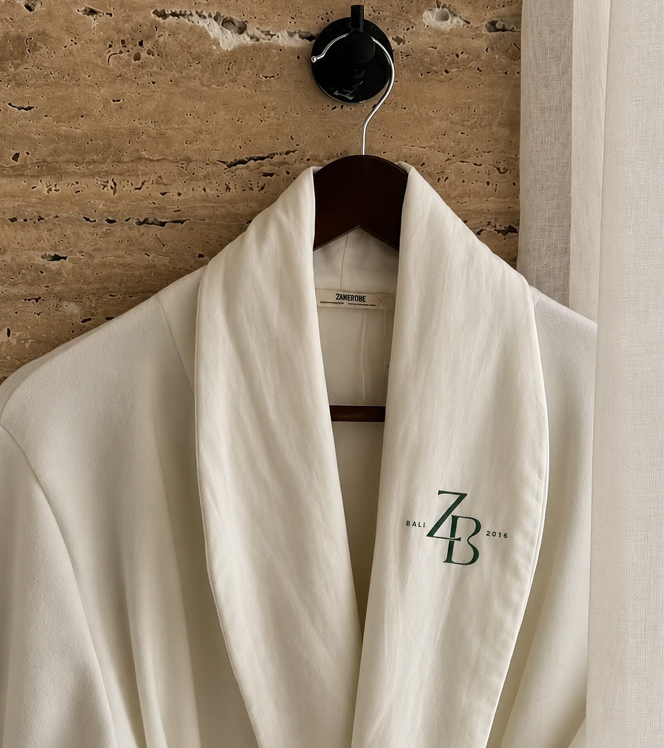 A white robe carrying the ZB monogram, hung on travertine