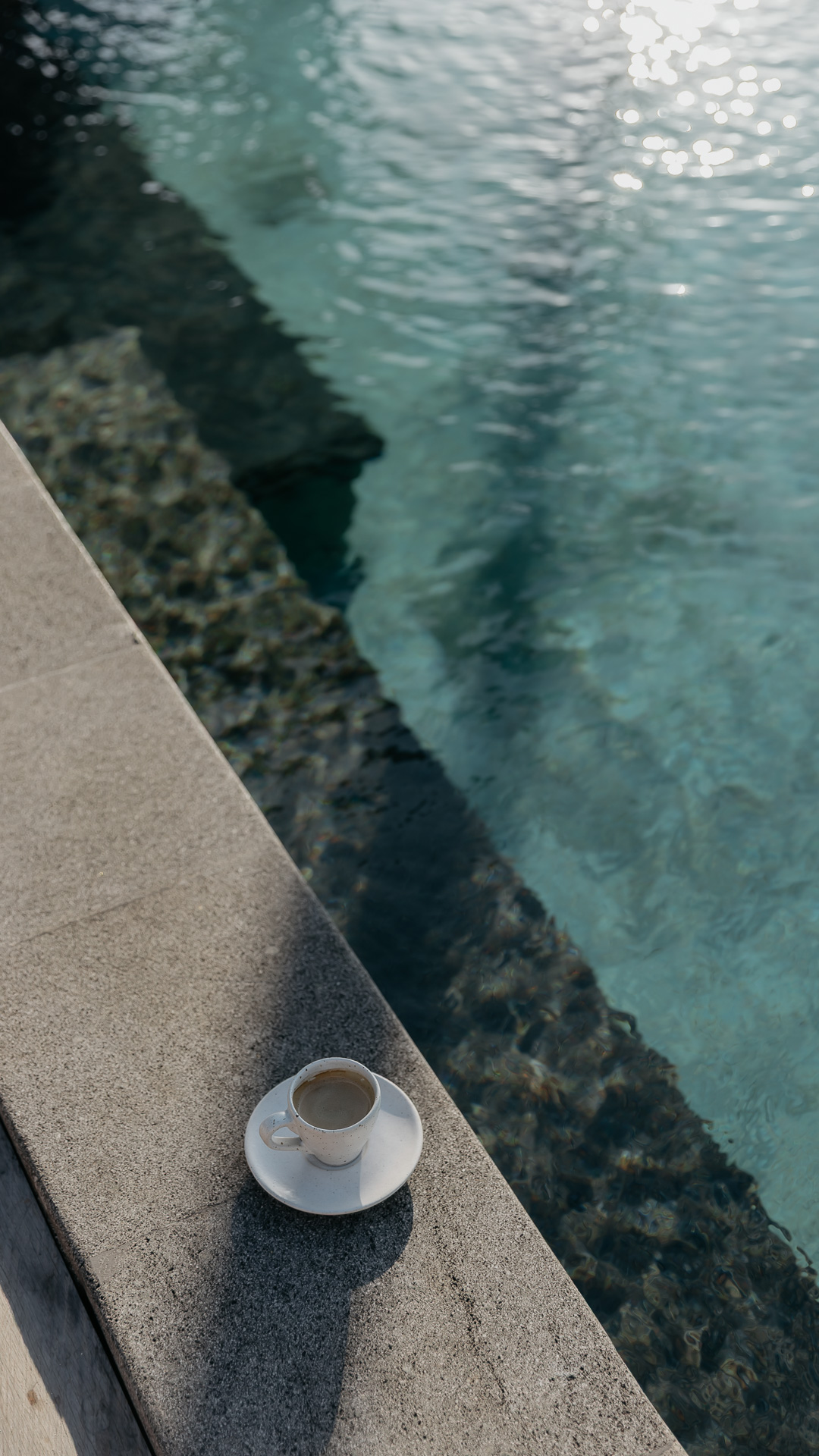 A coffee cup set on the pool edge at Zambala, morning light on the water